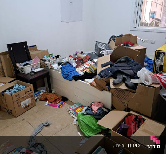 חדר מבולגן עם קופסאות קרטון, בגדים וספרים מפוזרים